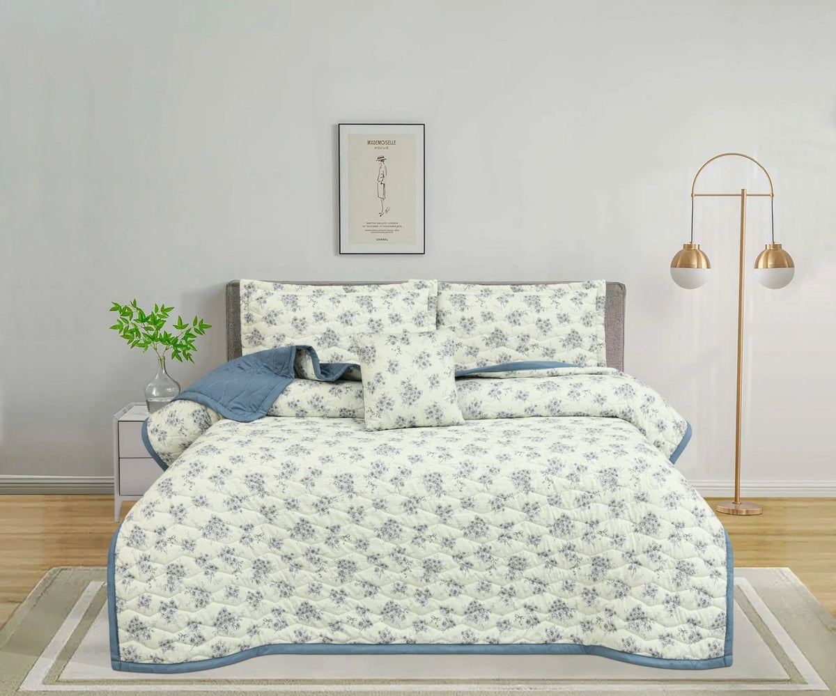White floral quilted bedspread set with blue trim and matching pillows on a bed
